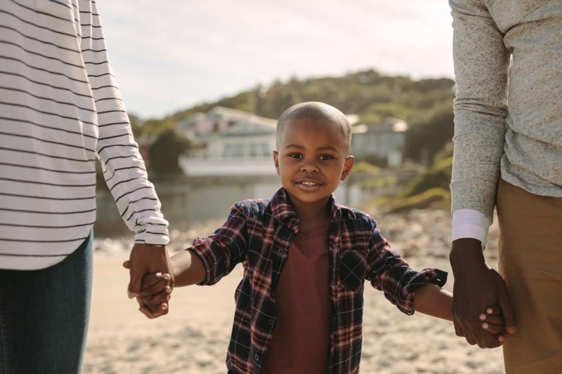 African American co-parenting a little boy in the middle both parent holding one of his hands.